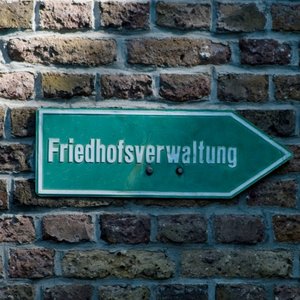 Grünes Schild an einer Mauer mit der Aufschrift Friedhofsverwaltung