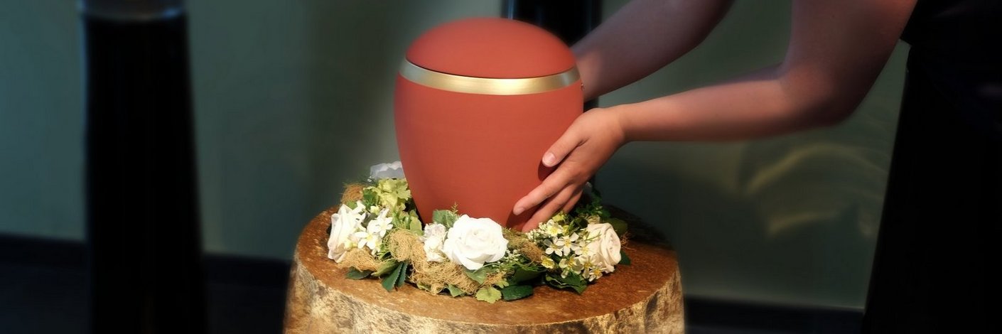 Frau stellt eine rote Urne auf einen mit Tuch und Blumen geschmückten Ständer