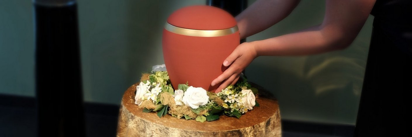 Frau stellt eine rote Urne auf einen mit Tuch und Blumen geschmückten Ständer