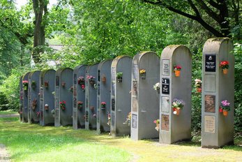 Urnenwand aus einzelnen grauen Stelen mit Abdeckplatten und Blumenschmuck