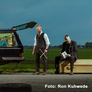 Zwei Bestatter mit Sarg, Leichenwagen und Reifenpanne