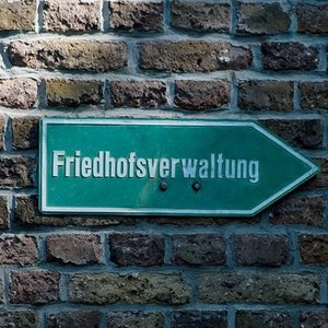 Schild mit der Aufschrift Friedhofsverwaltung an einer Ziegelmauer