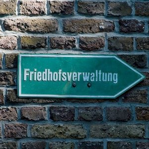 Schild mit der Aufschrift Friedhofsverwaltung an einer Ziegelmauer