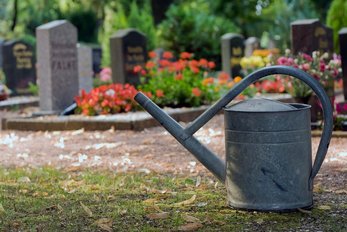 Graue Zink-Gießkanne vor Gräbern auf einem Friedhof