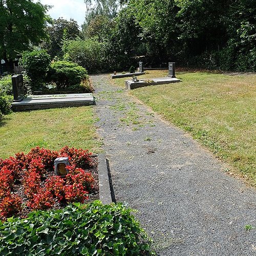 Einzelne Gräber auf fast leerer Fläche an einem Weg auf einem Friedhof