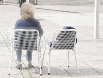 Frau auf Stuhl nebem leeren Stuhl