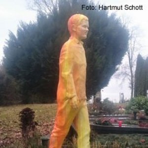 Statue eines jungen Mannes in gelber Farbe auf einem Grabmal