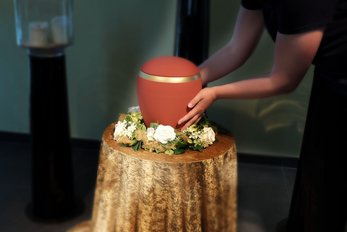 Frau umfasst eine rote Urne mit Blumenschmuck