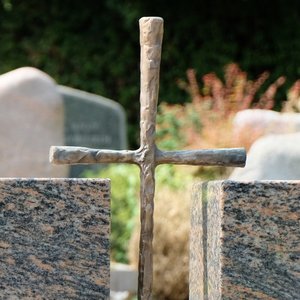 Kreuz aus Metall als Gestaltungselement eines Grabmals aus Stein