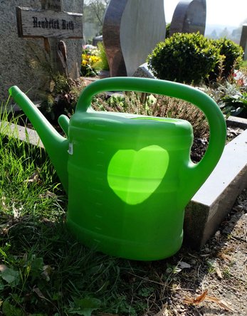 Eine grüne Gießkannevor einer Grabstelle auf einem Friedhof